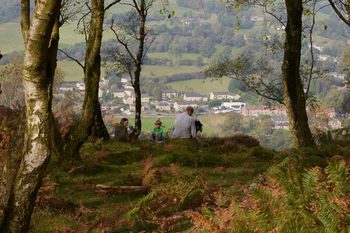 Picnic over Curbar Edge This landscape photograph shows a group of people enjoying a picnic on Curbar Edge, which is a rural escarpment in the Peak District, England, United Kingdom. The image was taken in the late morning during autumn, as indicated by the soft daylight and the presence of brown ferns on the ground. In the background, the view overlooks the village of Curbar and surrounding countryside. The elevated vantage point above Curbar Edge provides a broad perspective of the green fields, scattered houses, and trees typical of rural Peak District scenery. The photograph captures the essence of rural England, highlighting Curbar Edge as a scenic landmark above the local village.